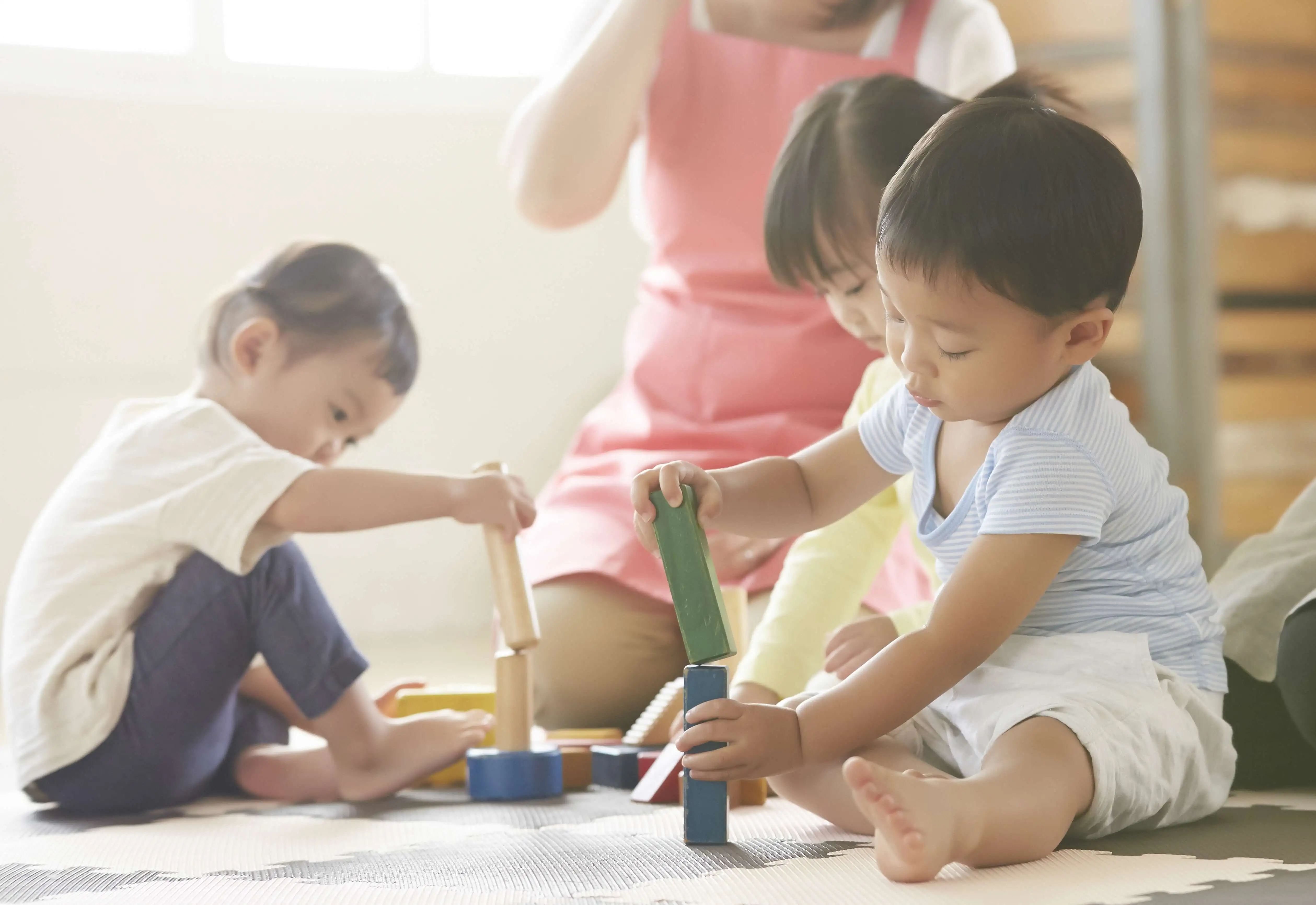 “保育士に見守られながら積み木で遊ぶ子供たち“